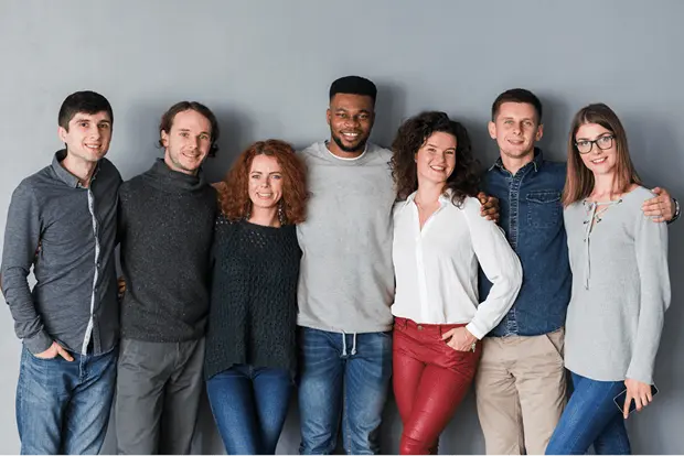 A photo of most of our team, posing arm and arm and smiling for the camera, before a gray background.
